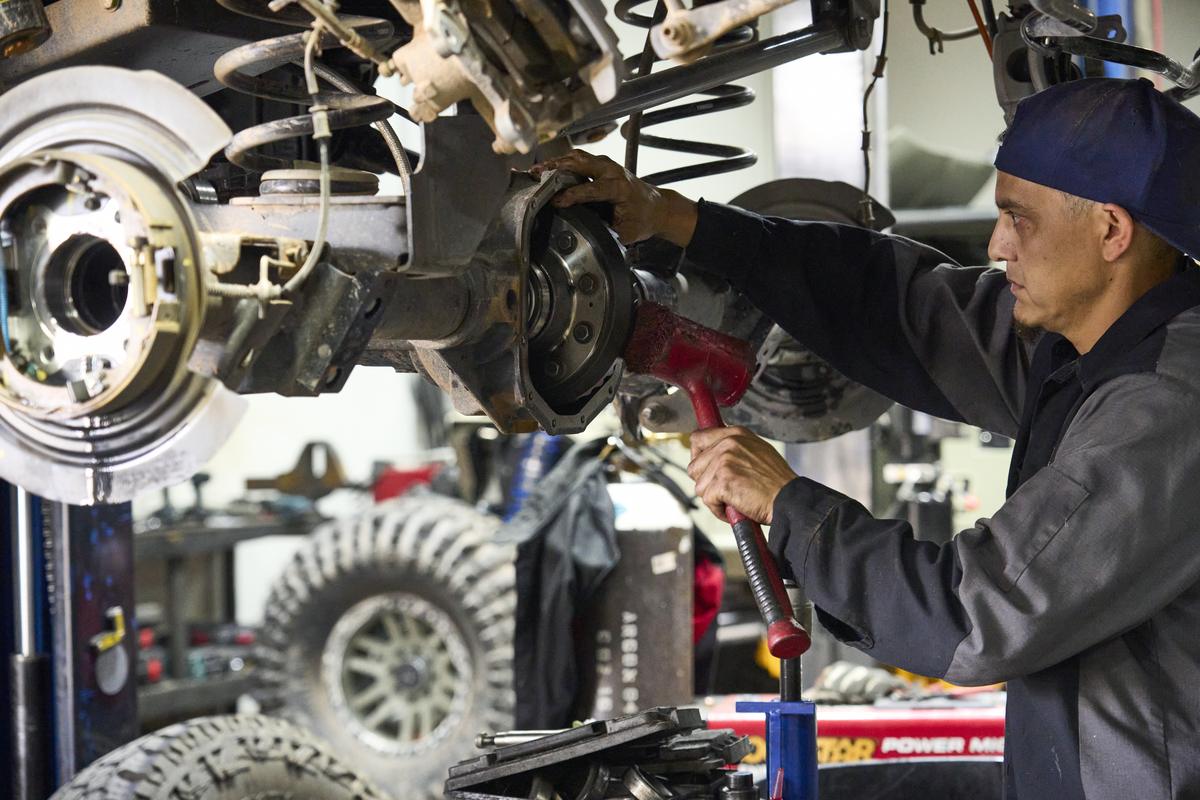 Technician working on the differential of a lifted truck on a shop lift while diagnosing a drivetrain noise