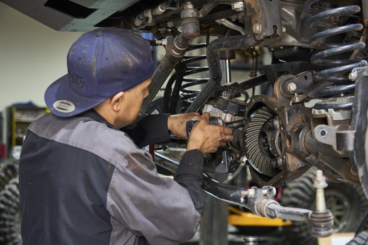 Technician inspecting the ring gear and carrier inside a differential housing with the cover removed on a lifted truck